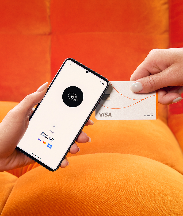 One hand holds a smartphone functioning as a card machine, displaying a contactless payment icon and a total of £35.00, while another hand taps a white Visa credit card to make the payment. The background is a bright orange sofa.