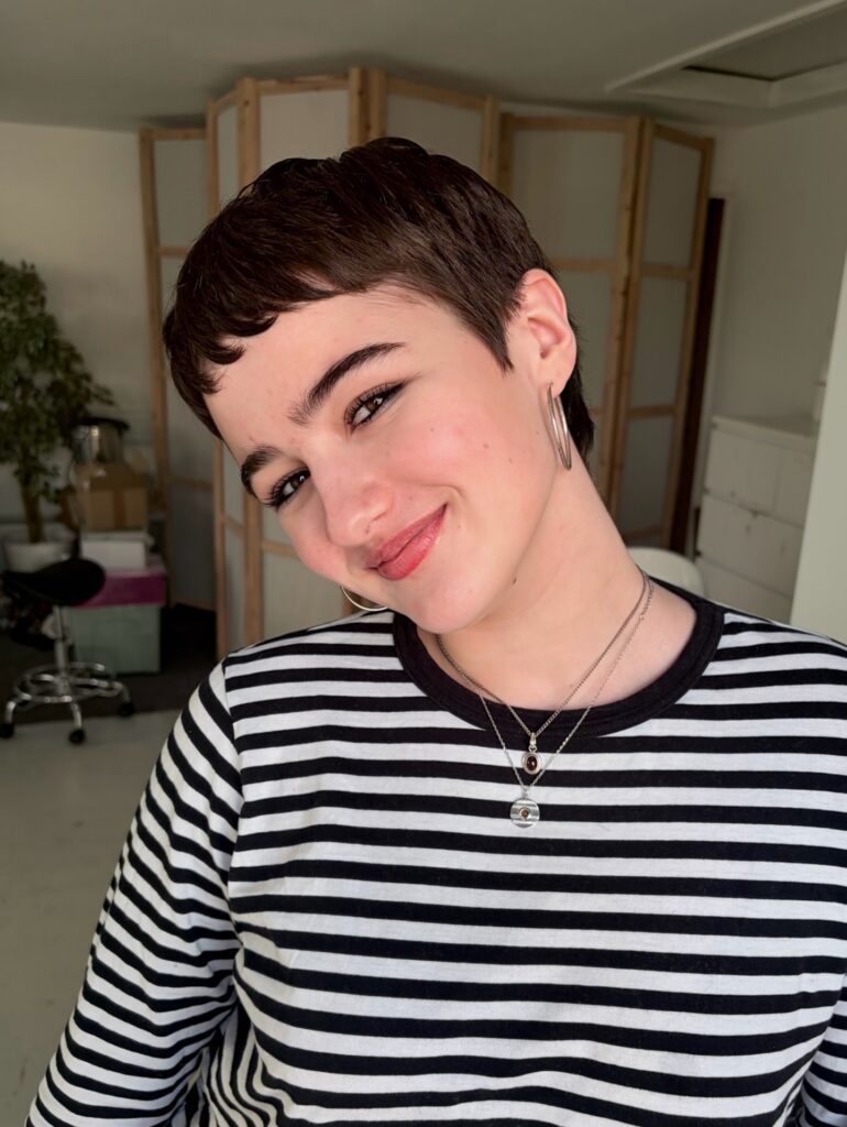 A person with a short dark pixie cut featuring micro bangs cut high above the eyebrows for a bold, fashion-forward statement.