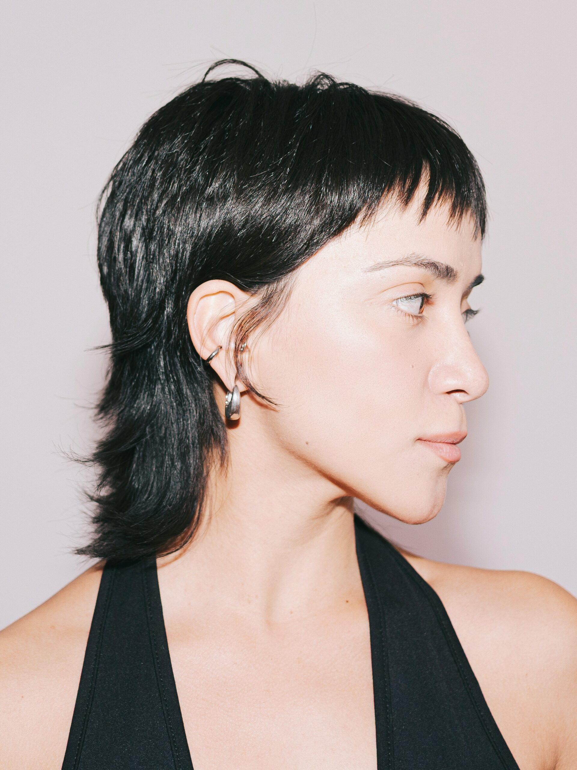 A young woman with a sleek mullet haircut wearing a black halterneck top.