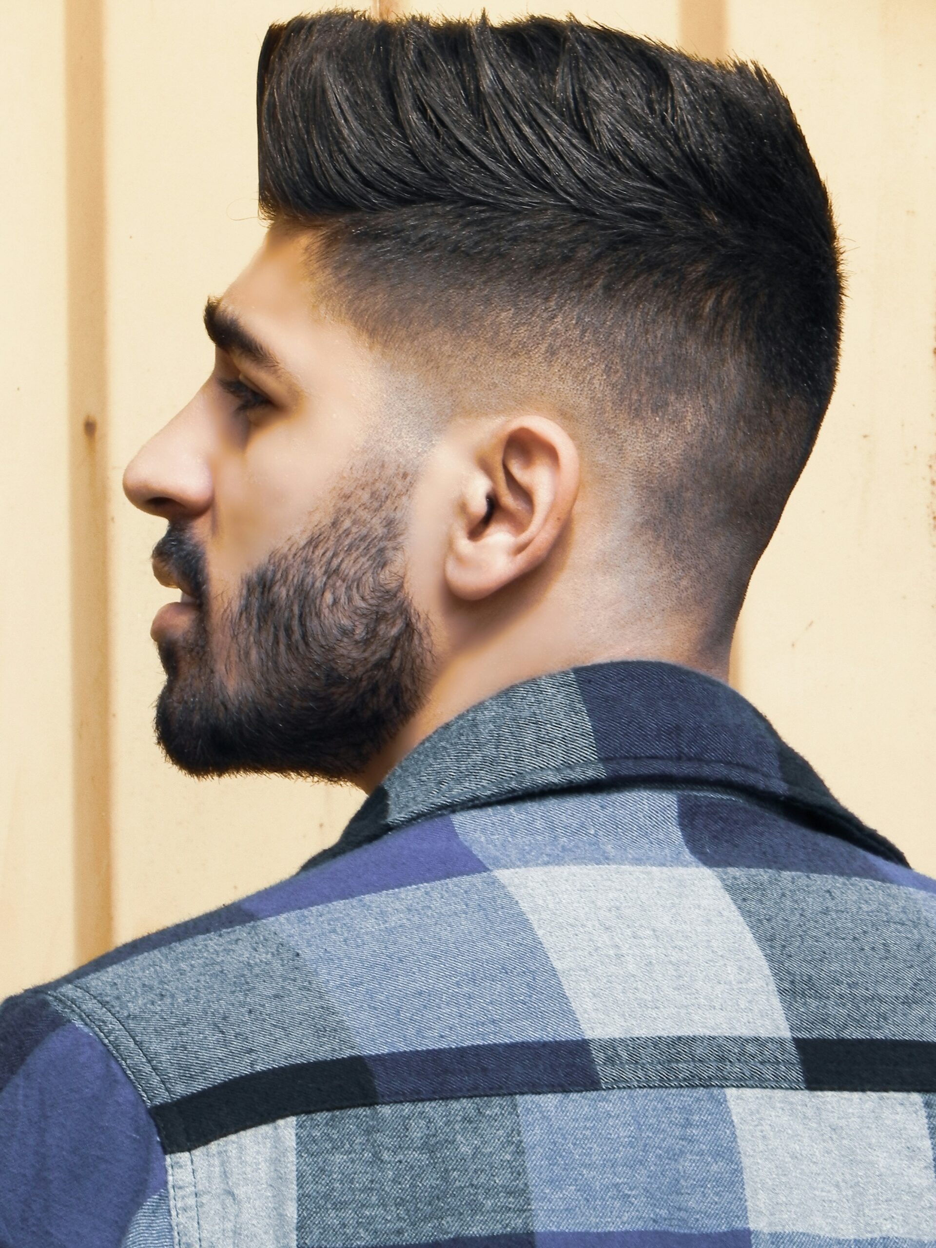 Side profile portrait of a man with a faux hawk hairstyle paired with a high taper fade