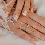 Classic white French tip manicure on natural square-shaped nails resting on white fabric