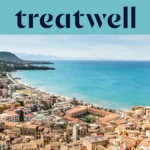 A sweeping view over a Sicilian coastal town, with terracotta-roofed old buildings, a crescent of sandy beach, clear turquoise sea and a rocky headland rising to one side.