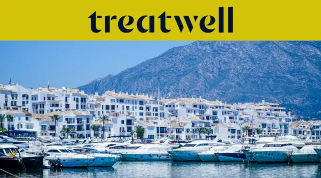 Puerto Banús marina in Marbella, lined with white apartment buildings and moored yachts against a mountain backdrop, beneath a yellow Treatwell banner.