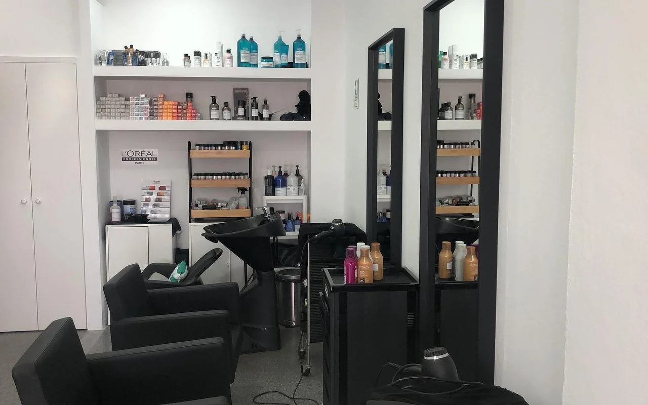 A hair salon with black washing chairs and basins, two tall slim wall mirrors, and shelves stocked with professional colour and hair-care products.