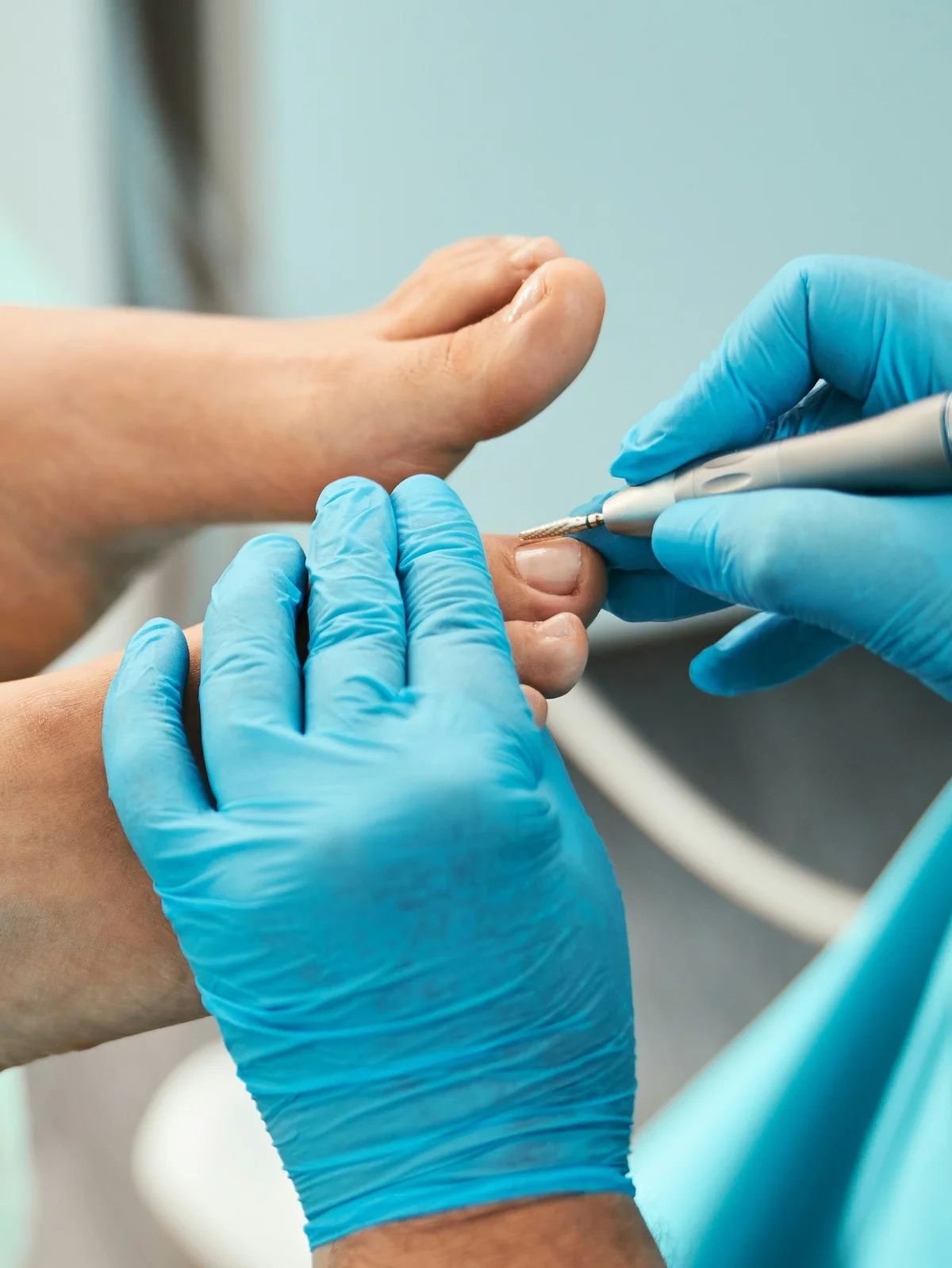 Close-up of a technician with a gloved hand using a small tool to tidy a client’s cuticles on their toes