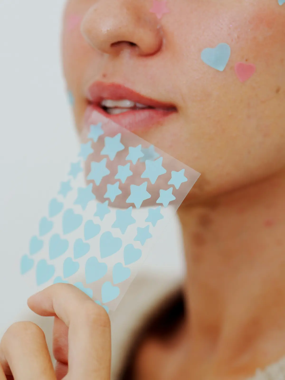 Close-up of a woman’s face with a few heart and star hydrocolloid patches covering spots