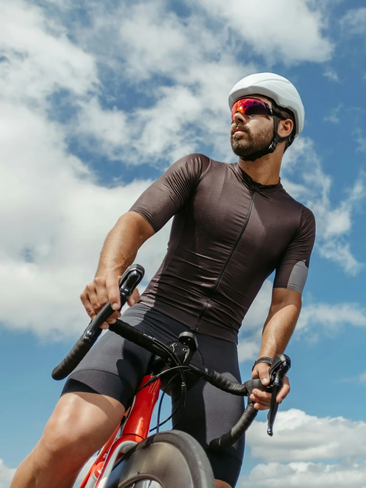 Shot from below, a male cyclist straddling his bike stops to look around under a blue sky with clouds