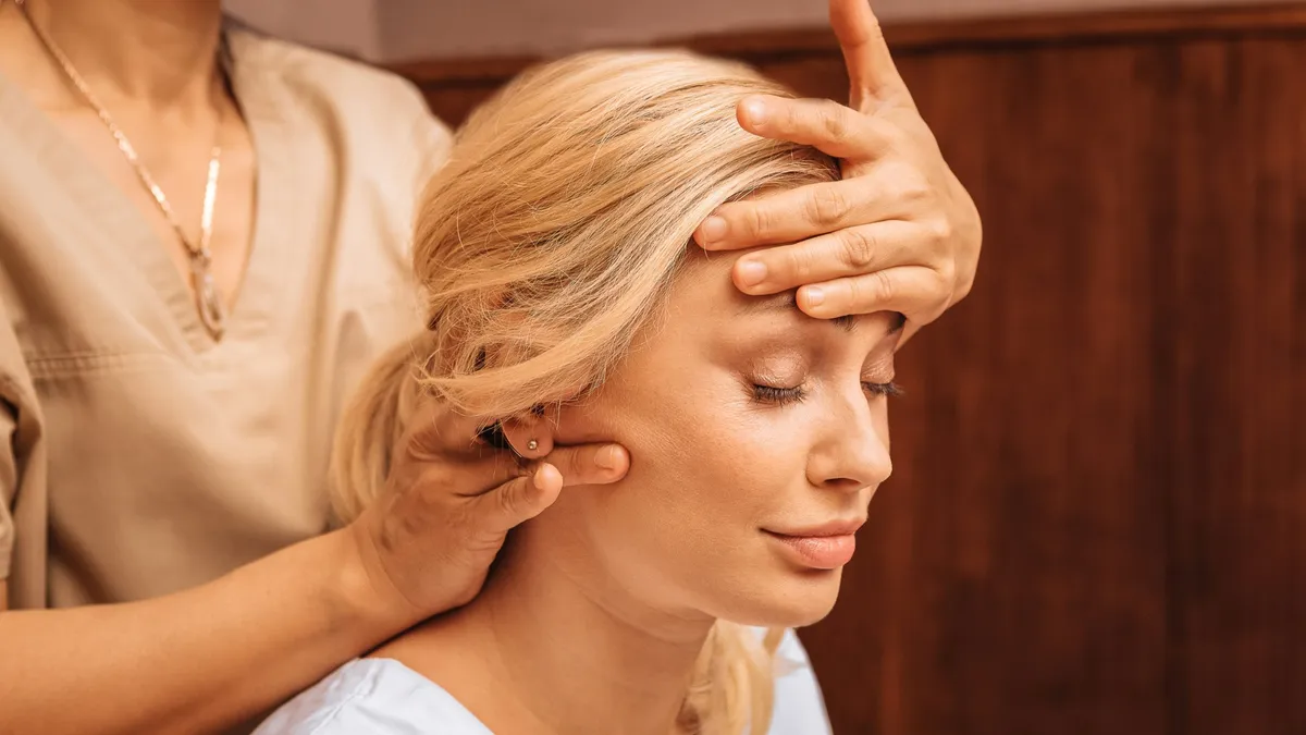 Close-up of a woman with her eyes closed as a therapist holds one hand on her forehead and massages her neck with the other hand during an Indian head massage